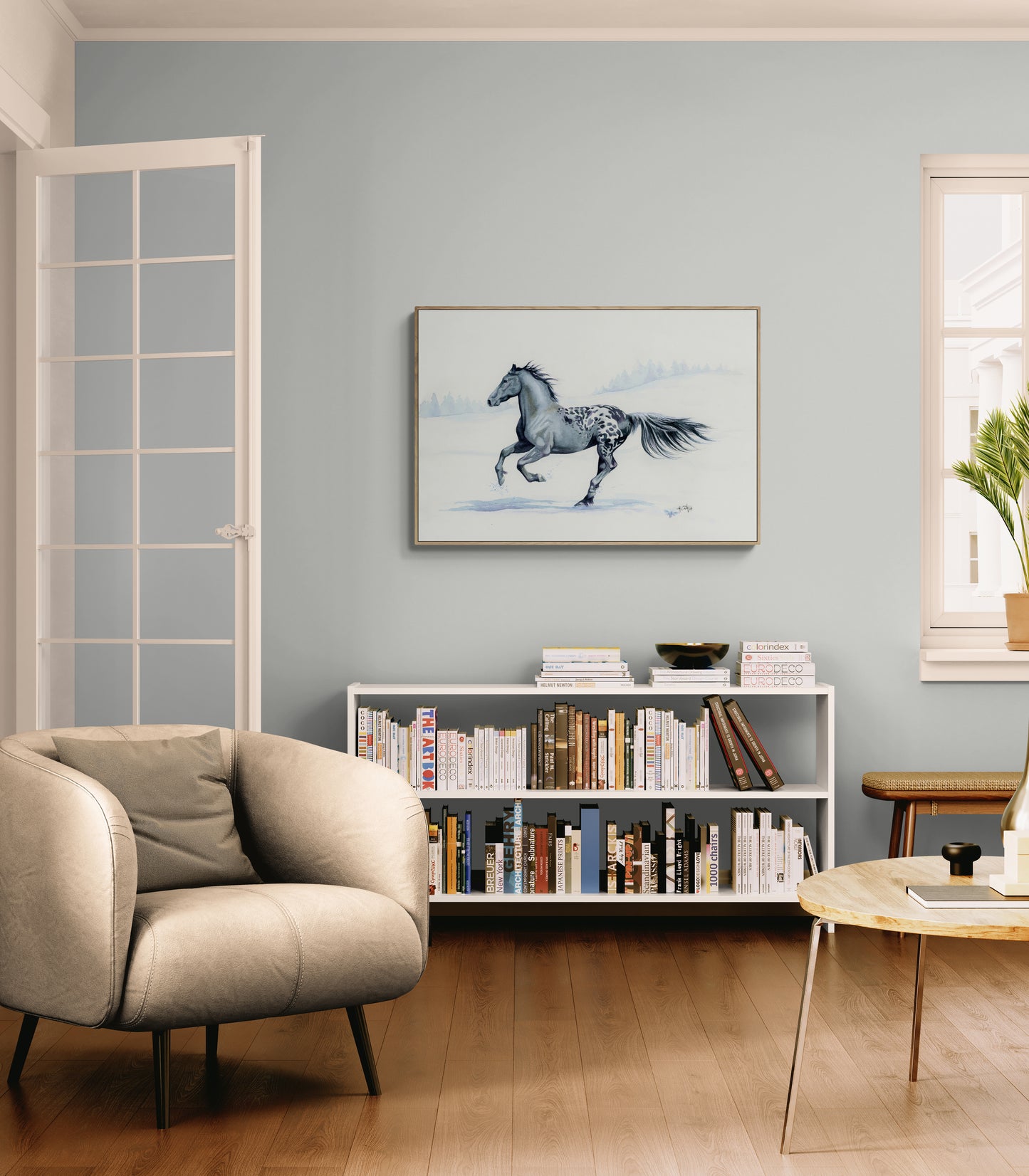 Living room with a beige armchair, bookshelf, and horse painting on the wall.